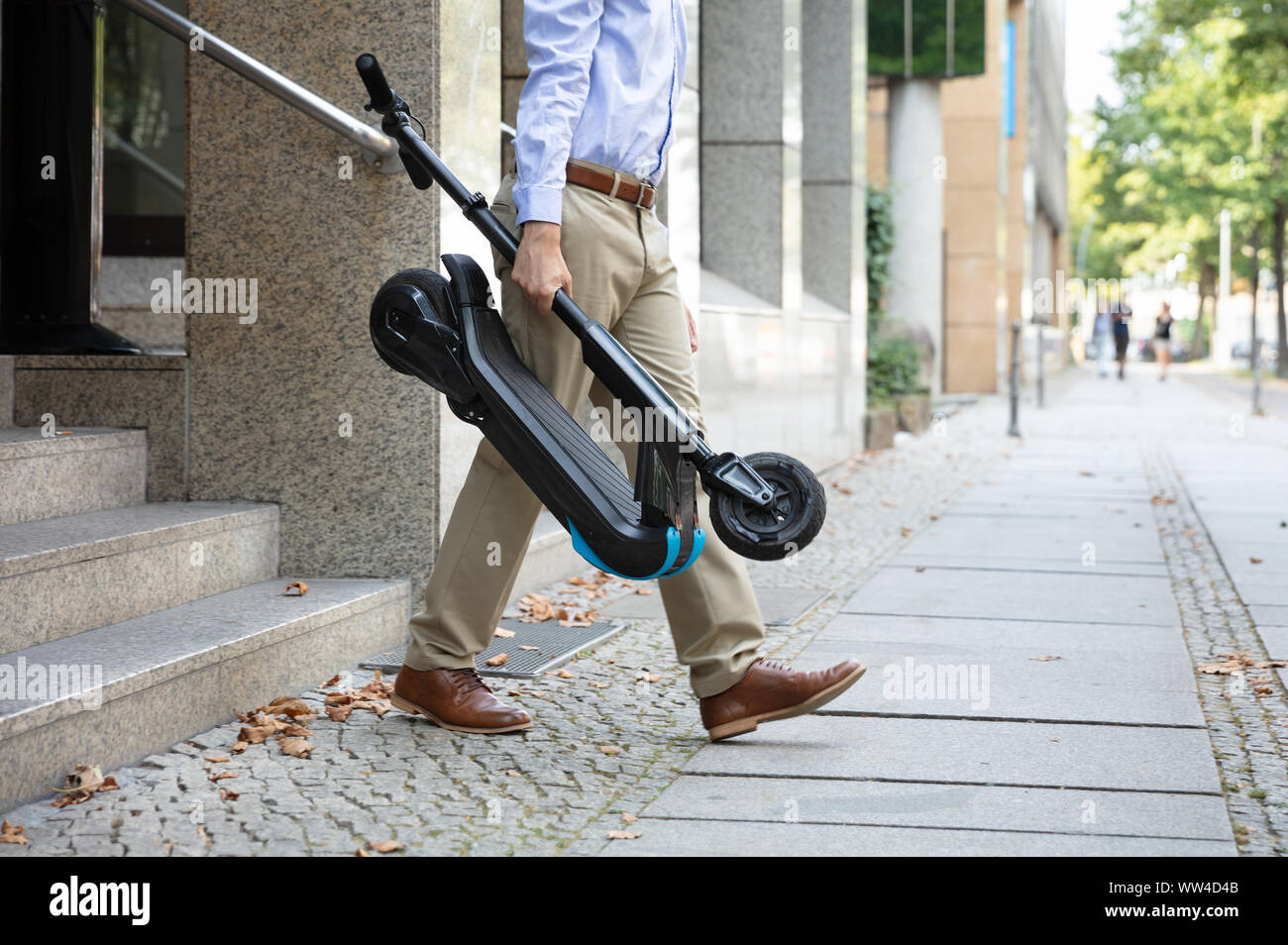 Homme portant l'E-scooter de travailler à la sortie de l'immeuble de bureaux Banque D'Images