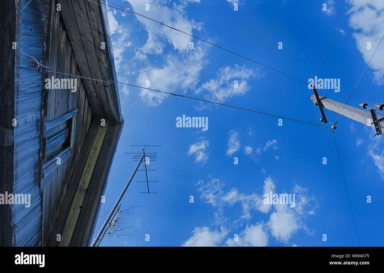 Toit d'une maison de campagne avec une vieille antenne de télévision et d'un poteau électrique avec des câbles à l'arrière-plan du ciel bleu Banque D'Images