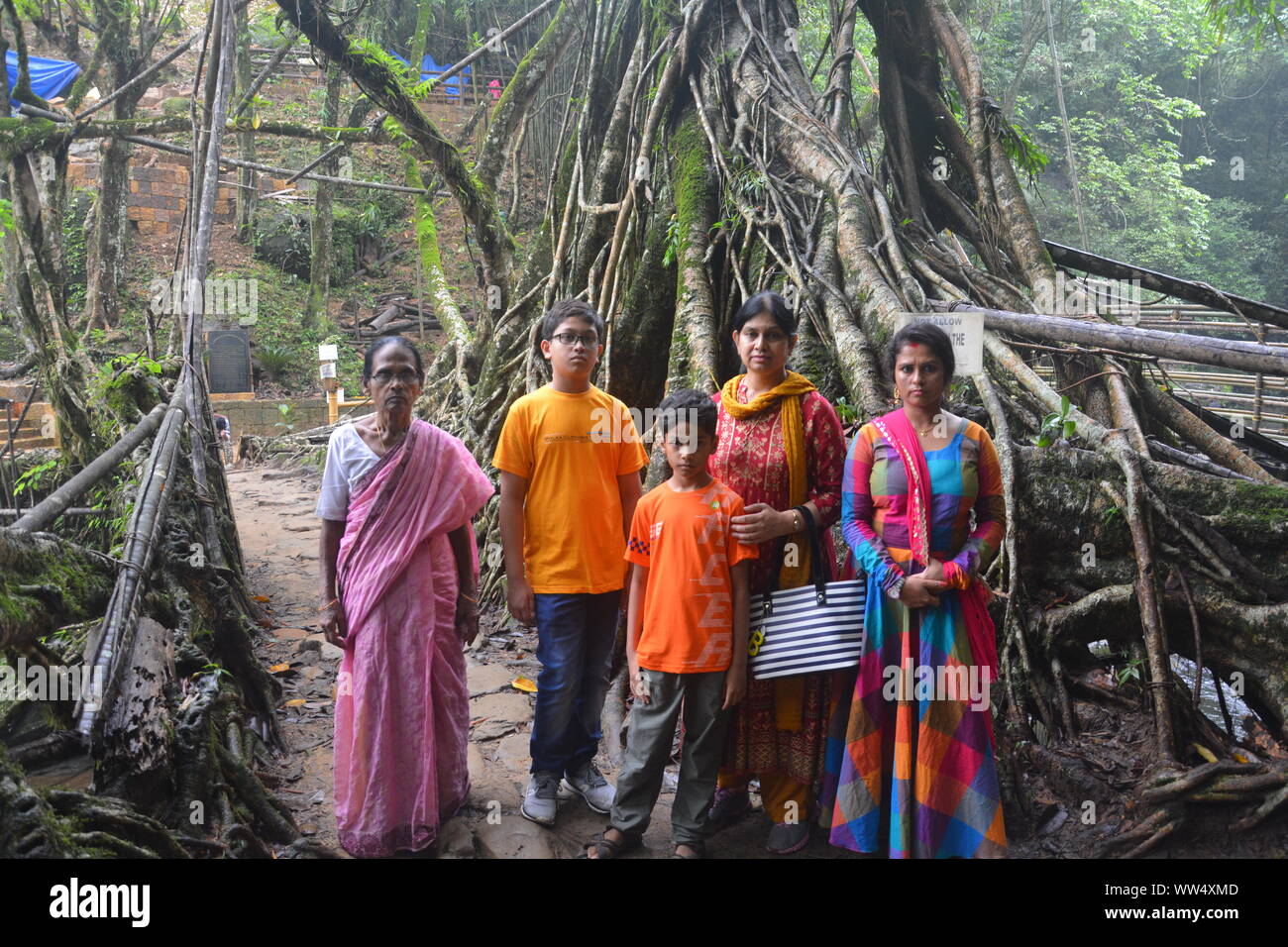 Une famille indienne composée de deux jeunes mères avec leurs deux jeunes garçons et une vieille dame debout sur le pont de racines vivantes dans Mawlynnong Cherrapu, Banque D'Images