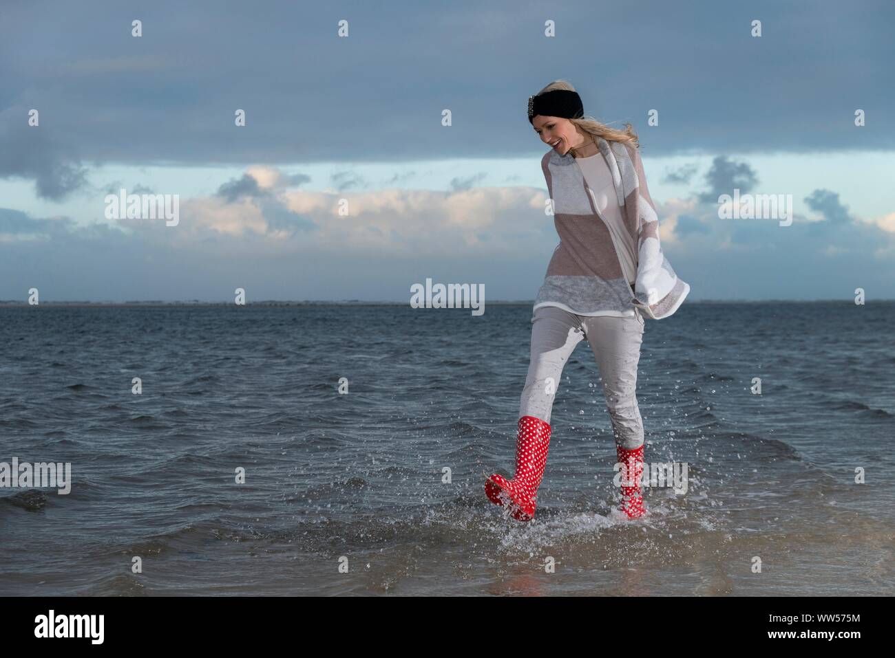 Femme avec des bottes rouge qui traverse l'eau à la mer Banque D'Images