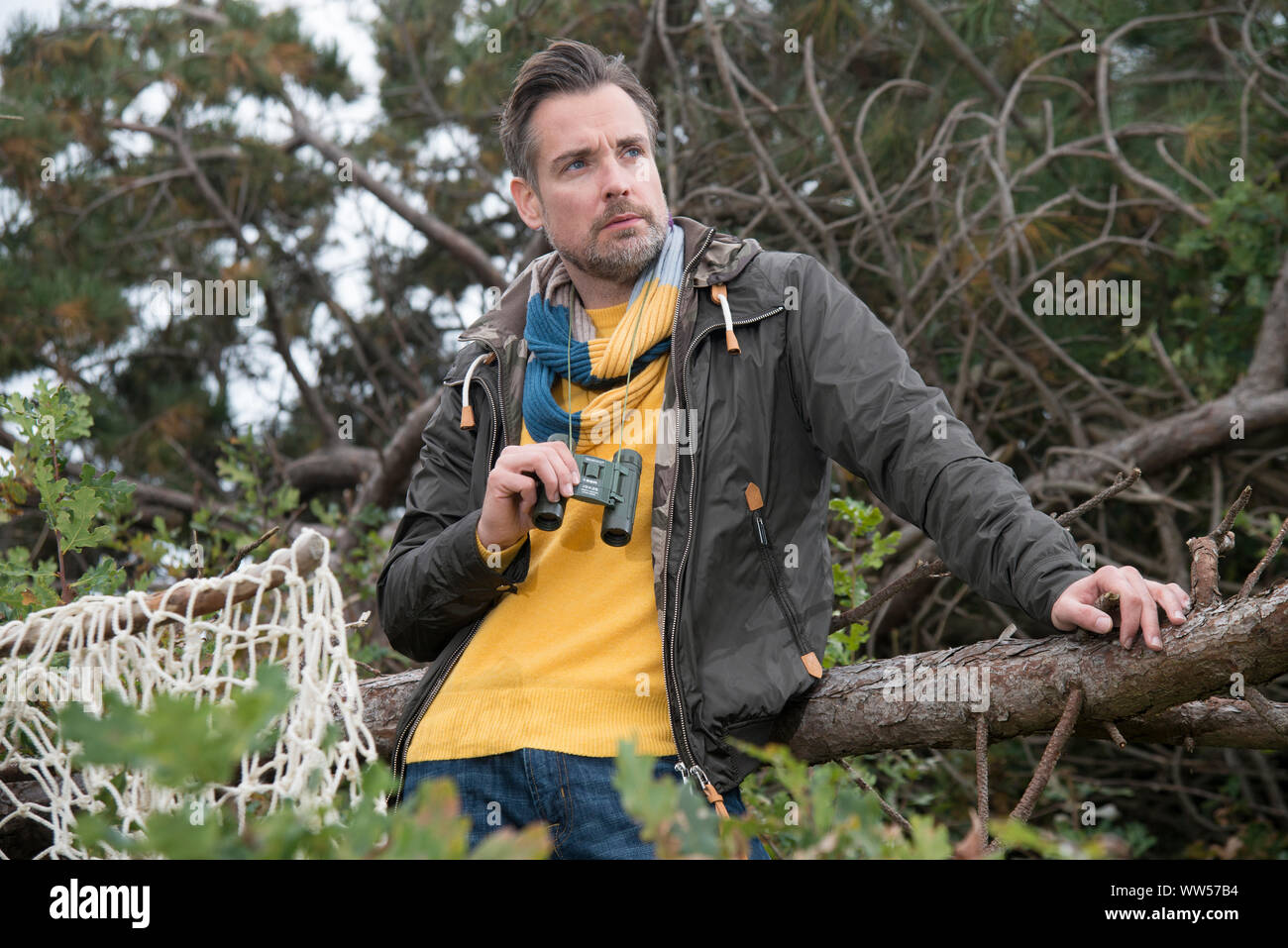 Homme avec des jumelles et pull jaune regardant au loin Banque D'Images