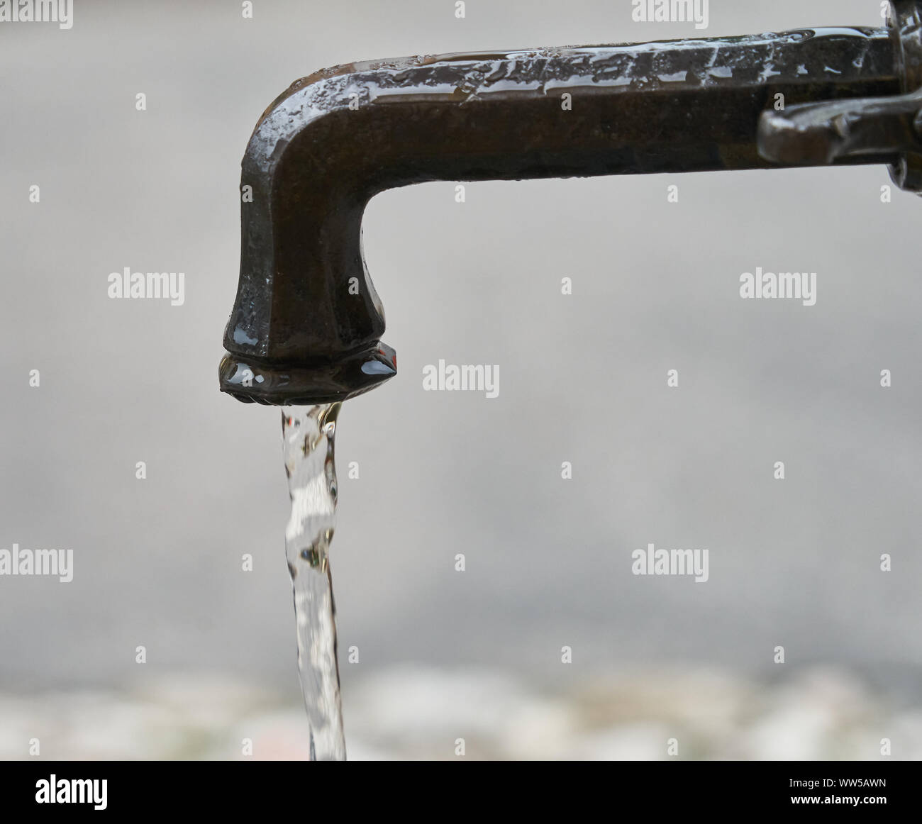 Image minimaliste d'un robinet antique d'où le calme et l'eau claire s'écoule lentement, contre un arrière-plan gris. Banque D'Images