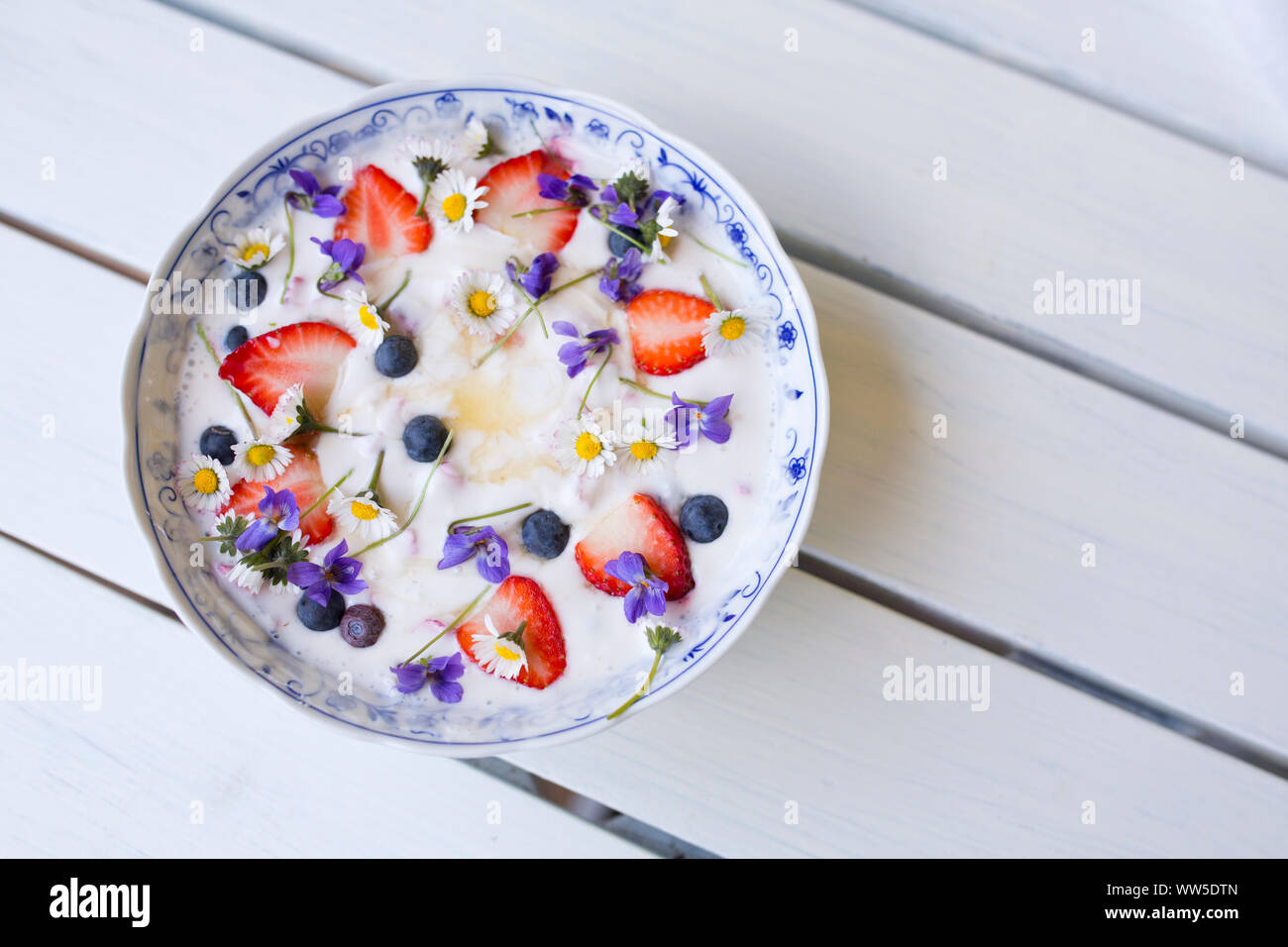 Le yogourt aux fraises, bleuets et fleurs sur table en bois blanc Banque D'Images