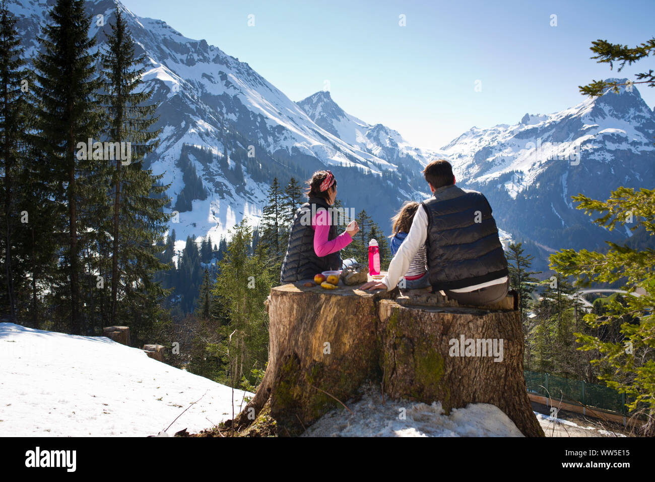 Père, mère et enfant avoir pique-nique sur un tronc, à la vue du paysage de montagne Banque D'Images