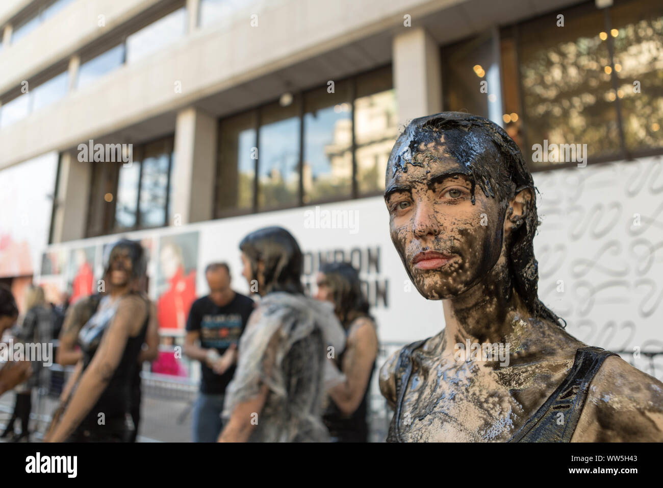 Londres, Royaume-Uni. 13 septembre 2019. Des activistes couverts de liquide noir protestent contre la production de cuir devant un lieu de la Fashion week de Londres. Un démonstrateur tient une pancarte indiquant « DUMP LEATHER » tandis que d'autres se tiennent vêtus de vêtements noirs sur une surface tachée de la même façon. La manifestation met en lumière les préoccupations éthiques et environnementales entourant l'utilisation du cuir dans la mode. Penelope Barritt/Alamy Live News Banque D'Images