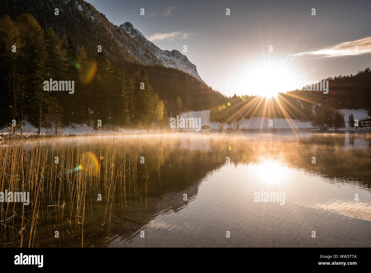 Situation de contre-jour du soleil couchant avec de forts rayons de soleil et reflet dans l'eau d'un petit lac de montagne alpine. Banque D'Images