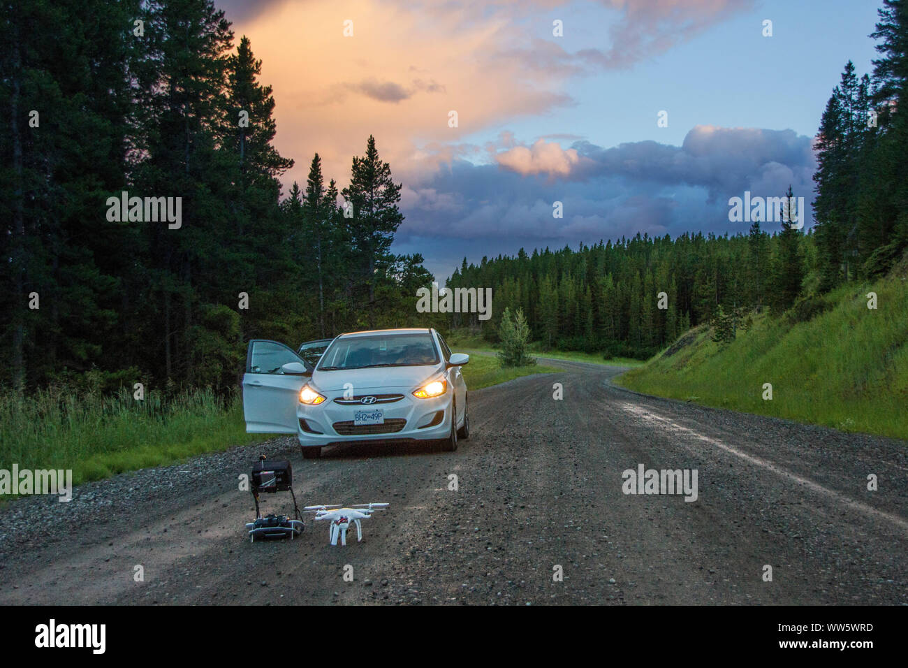 Voiture sur une route de gravier, au crépuscule, un multicopter prêt à décoller Banque D'Images