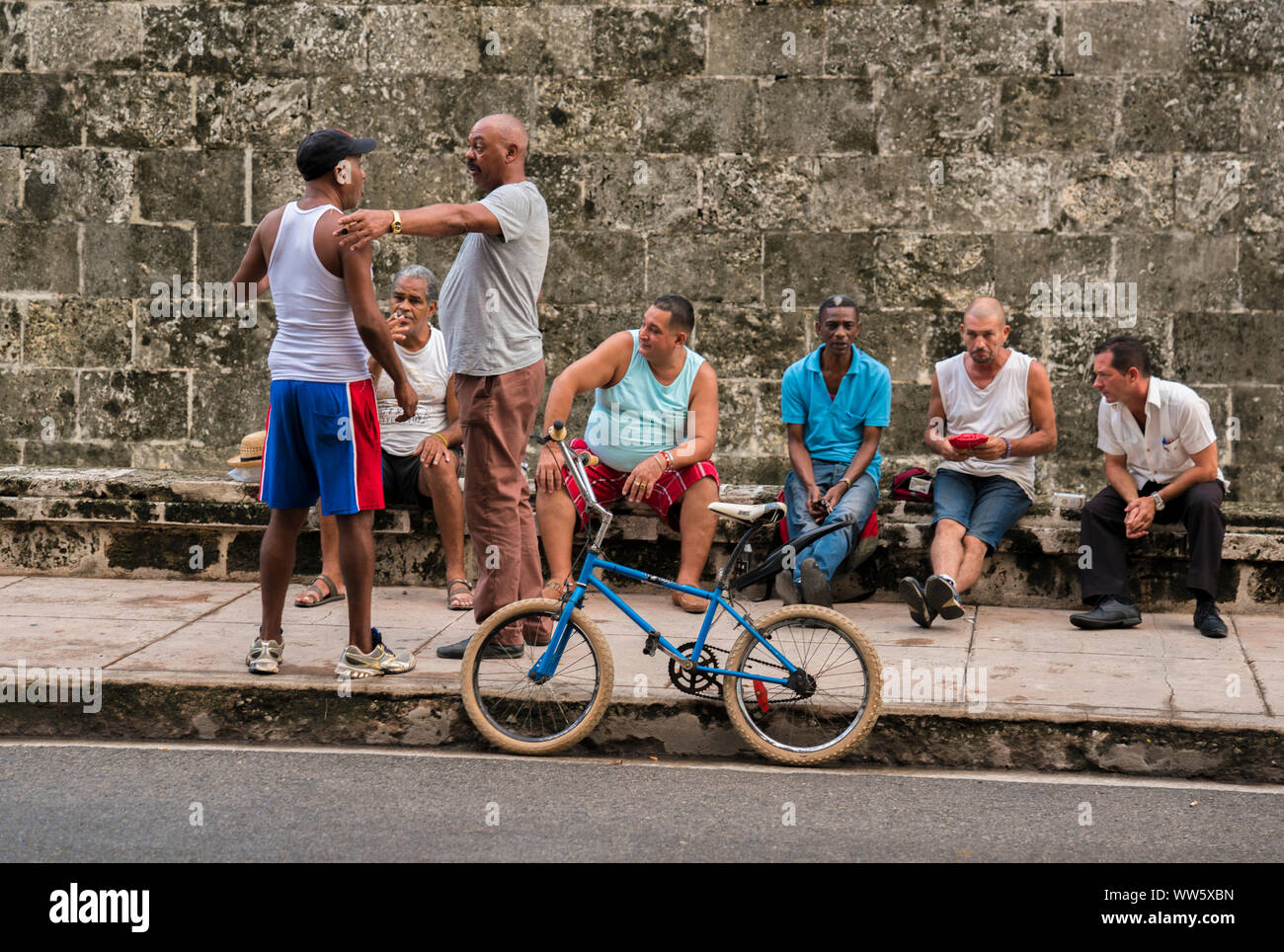 Groupe d'hommes assis sur un mur et à parler, deux hommes debout, vélo BMX Banque D'Images