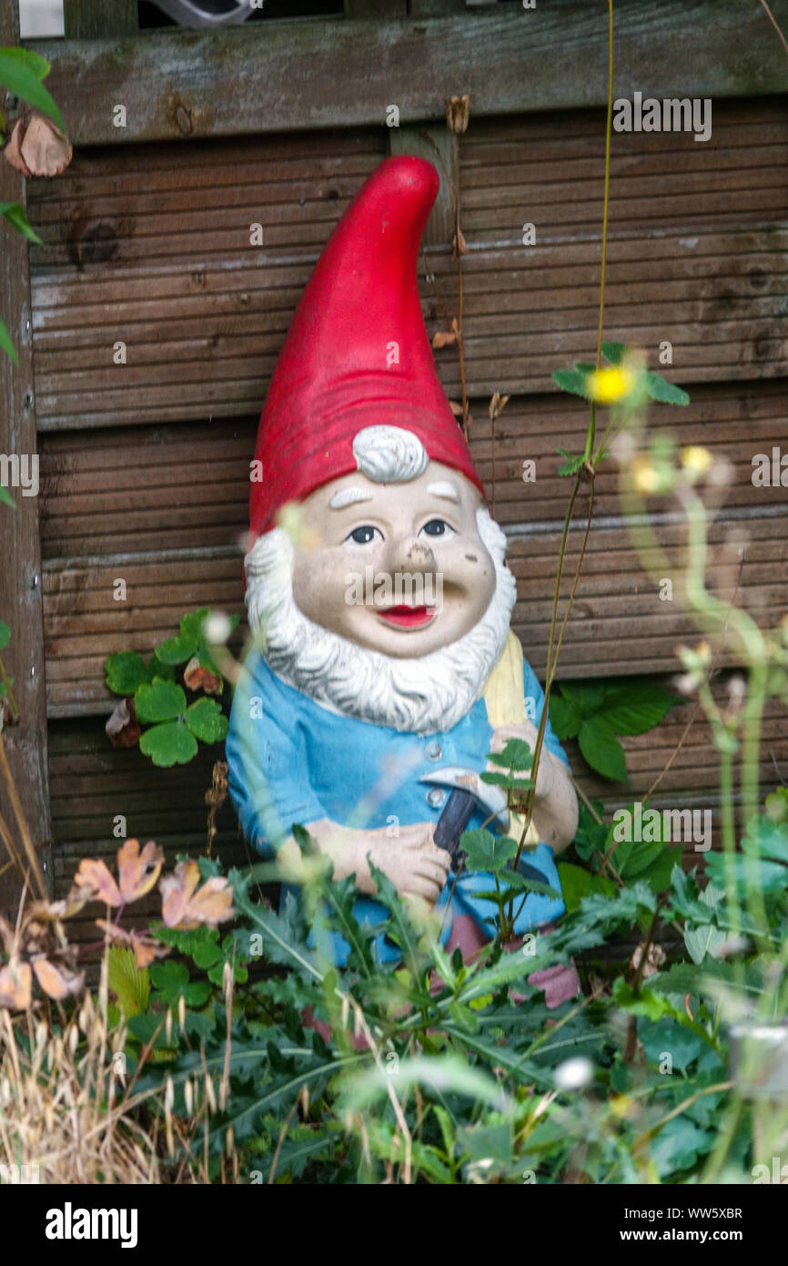 Gnome de jardin allemand appuyé contre le compost mural, en capuchon rouge et seul Banque D'Images