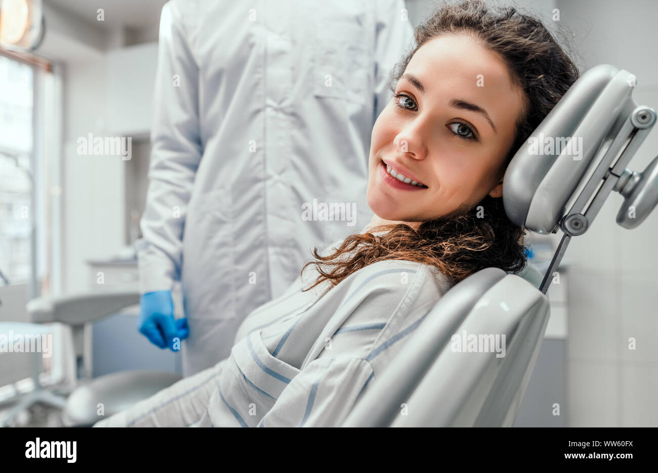 Jeune femme assis sur une chaise dans le cabinet dentaire. la préparation pour l'examen dentaire. En regardant la caméra. Banque D'Images