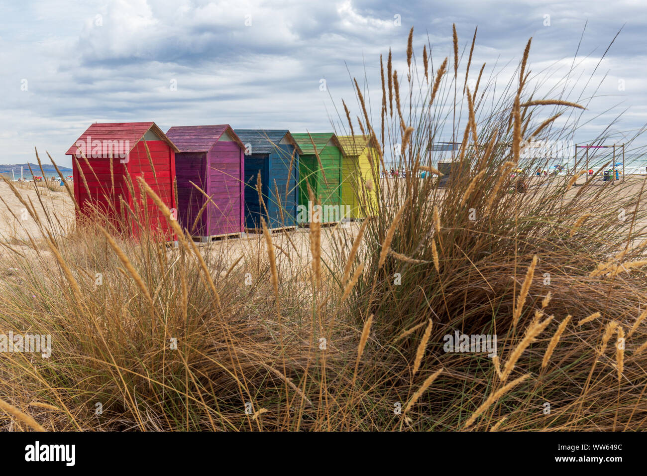 Changer de maison coloré dans la rangée visible au travers de l'herbe jaune tiges. Snd plage et mer et montagnes en arrière-plan Banque D'Images