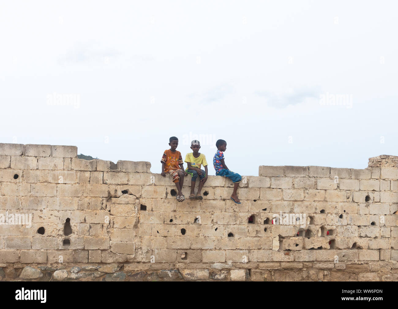 Les garçons de l'Érythrée s'asseoir sur un mur avec des trous de balle, Debub, Ghinda, Erythrée Banque D'Images