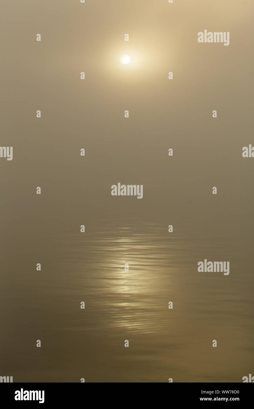 Lever de soleil brumeux avec un soleil atténué reflété sur l'eau calme à Honeymoon Island Causeway à Dunedin, Floride. Banque D'Images