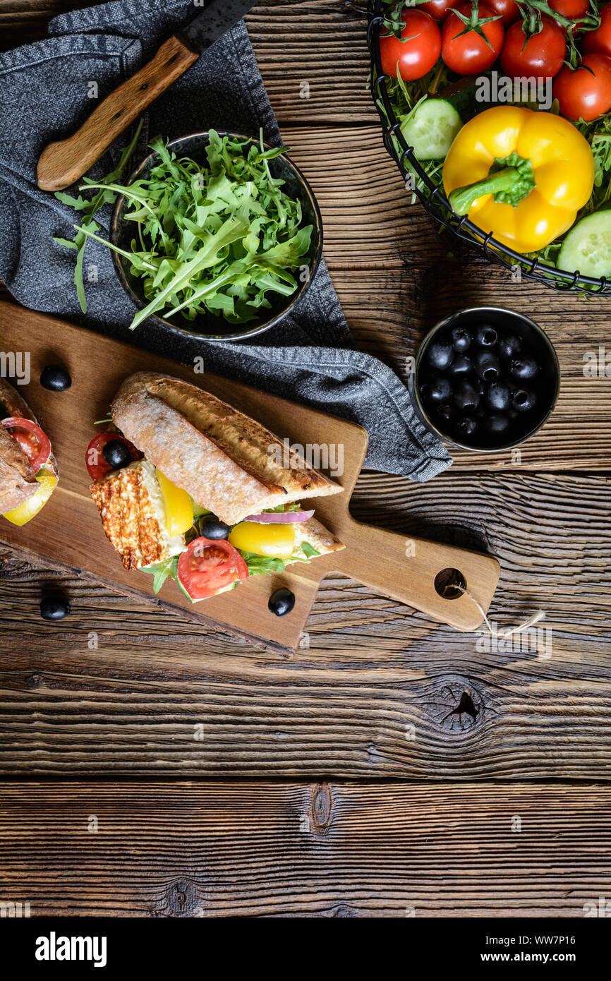 Végétarien complet baguette farcie de fromage blanc grillé, roquette, tomates, olives noires, poivrons et oignons rouges sur fond de bois Banque D'Images