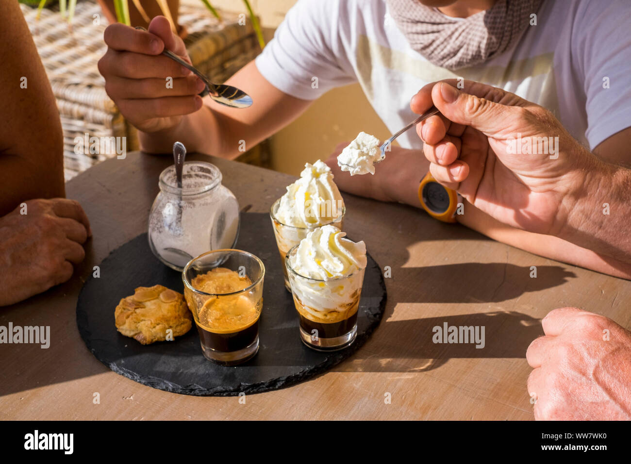 3 personnes à la table sur la terrasse, prendre le petit déjeuner avec café, crème et les cookies dans la chaleur de l'été soleil Banque D'Images