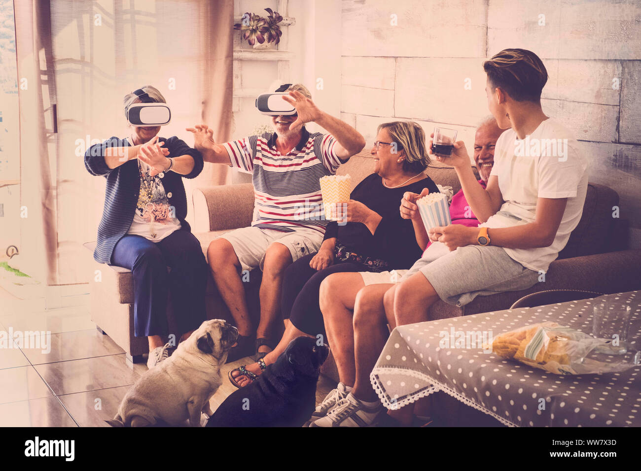 Un adolescent et grands-pères à la maison faisant paty avec pop-corn et lunettes payer casque avec rire et sourire. Deux carlin chien de s'asseoir sur le sol. Tons vintage marron chaud Banque D'Images