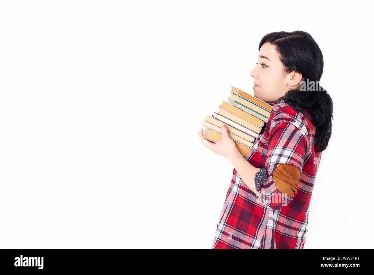 Une jeune fille élève dans une chemise à carreaux rouge tenant une pile lourde de livres anciens ou de manuels. Préparation à l'admission à l'université, à une session ou à des examens. Banque D'Images