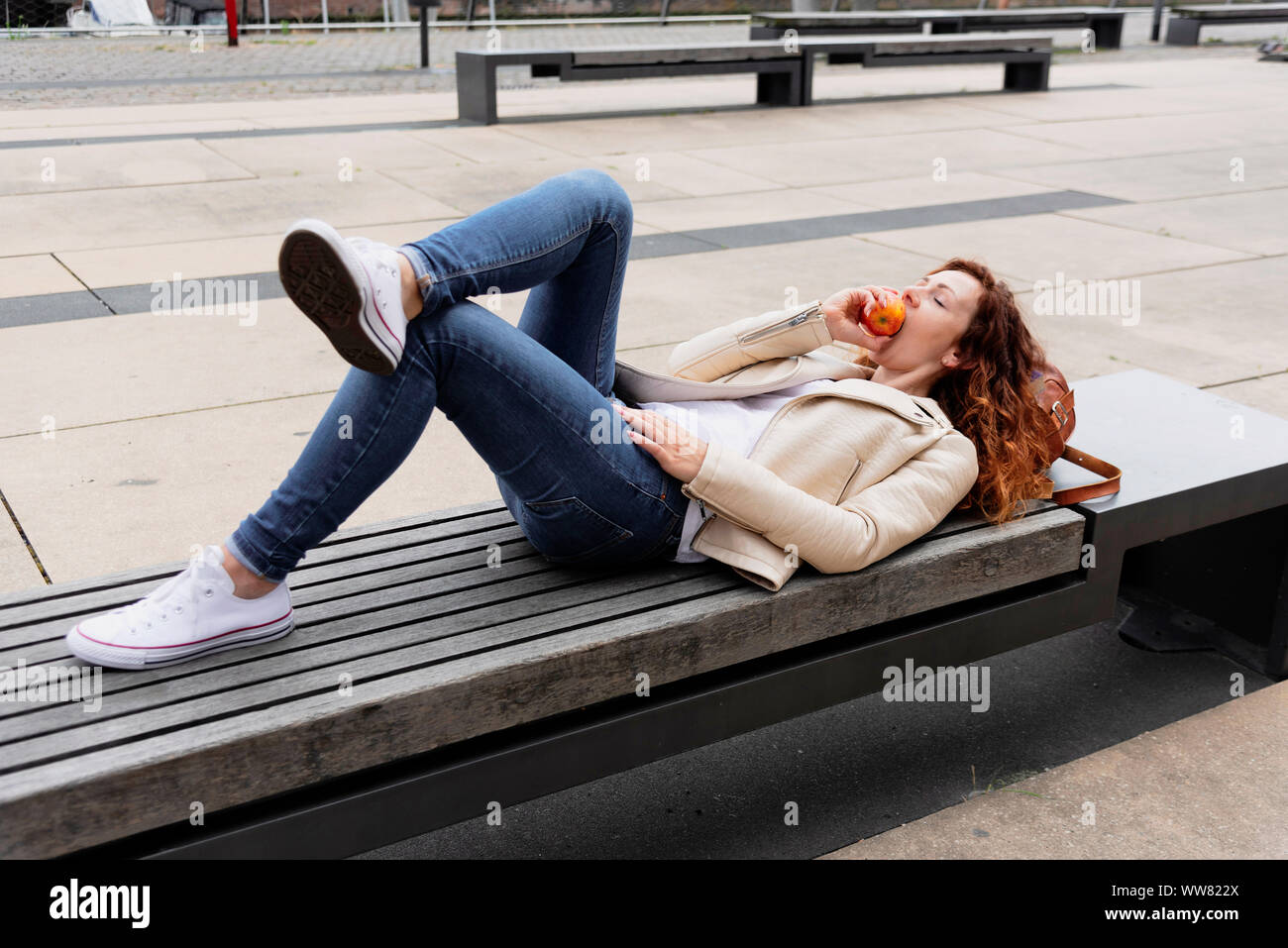 Jeune femme allongée sur un banc et croquer dans une pomme Banque D'Images