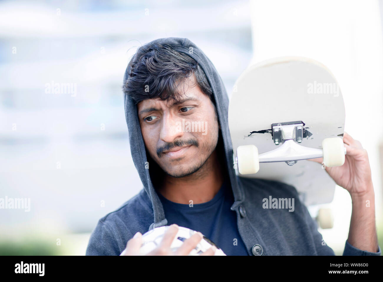 Jeune homme avec hoodie holding skateboard et ball Banque D'Images