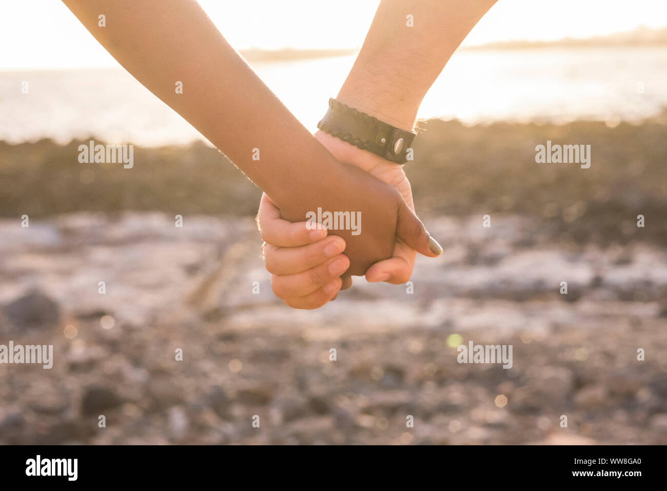 Concept d'amour avec la main en noir et blanc de toucher et prendre en face de l'océan lors d'un coucher du soleil doré, lumière chaude et jaune pour représenter la vraie relation avec les gens de races différentes Banque D'Images