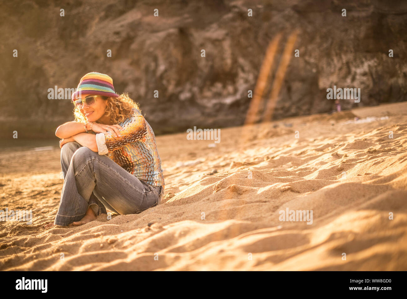 Jolie jeune femme s'asseoir sur le sable à la plage, se relaxer et apprécier le coucher du soleil et ensoleillée journée de vacances, séjour bien dans un lieu naturel et d'une activité de loisirs concept, les vêtements clairs Banque D'Images