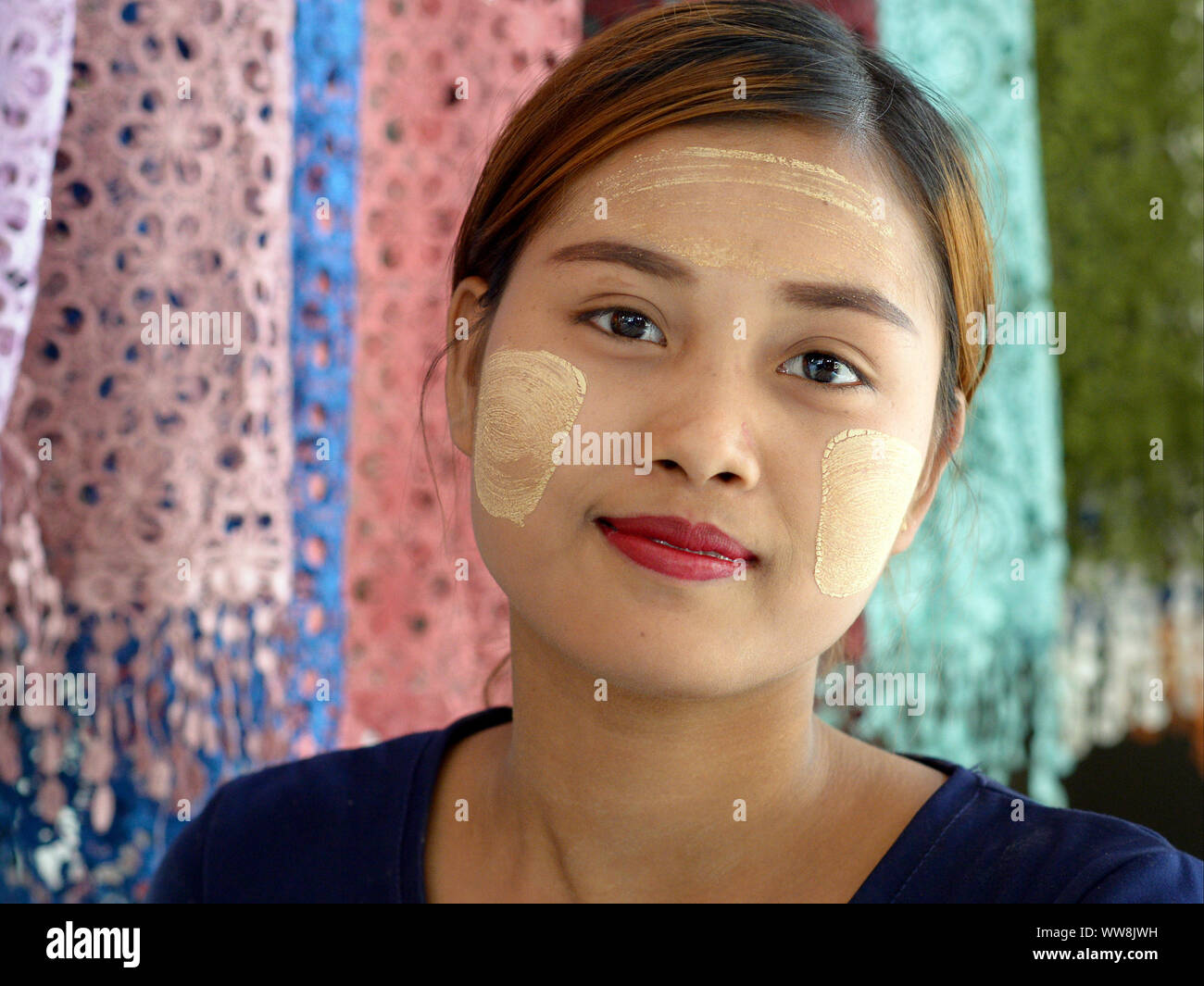 Jeune femme birmane avec des taches de blanc jaunâtre visage traditionnel thanaka cosmetic sur le front et les joues pose pour la caméra. Banque D'Images