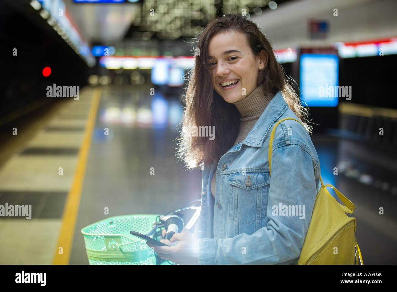 Adolescentes en jeans avec sac à dos jaune et vélo debout sur la station de métro, l'attente pour le train, sourire et rire. La station de métro futuriste Banque D'Images