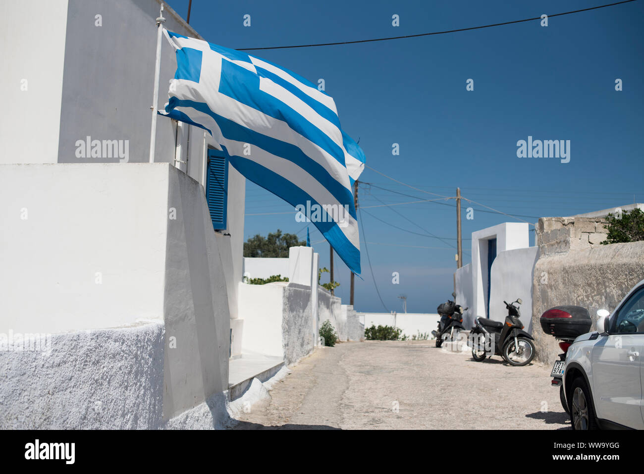 Santorin, Grèce - 25 juin 2018 : un drapeau grec souffle dans le vent à l'extérieur d'une maison traditionnelle de la ville de Pygros sur l'île de Santorin. Banque D'Images