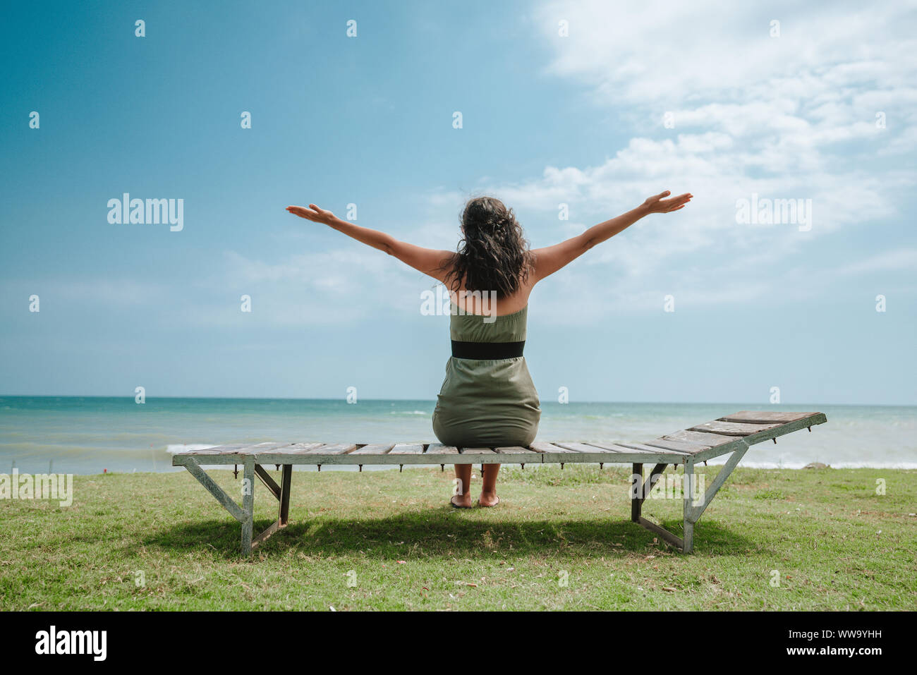 Jeune femme assise sur la plage et bras levés Banque D'Images