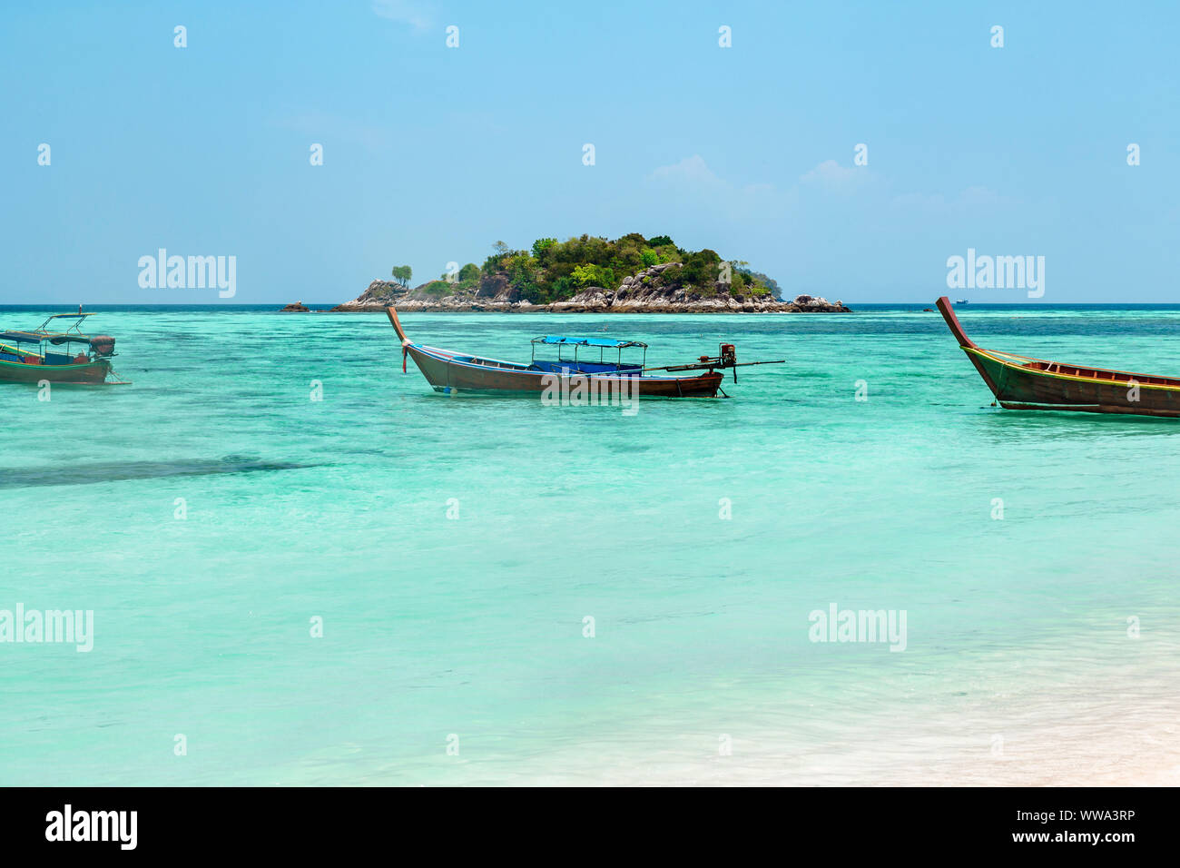 Bateau en bois traditionnel thaïlandais amarré dans un lagon protégé avec crystal clear bleu étincelant de l'eau avec une île en arrière-plan, Koh Lipe, Banque D'Images