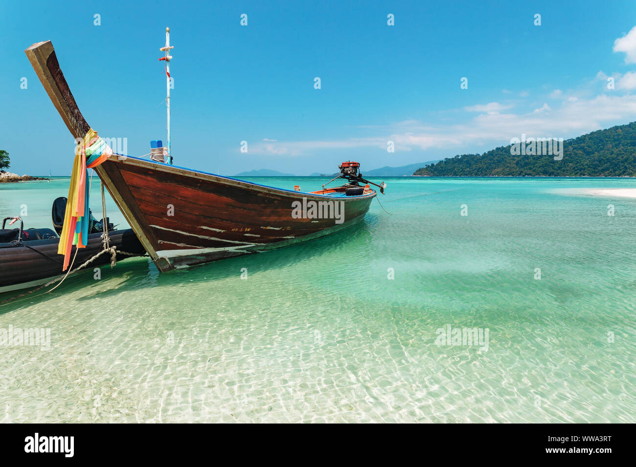 Bateau thaï traditionnel en bois avec tissu coloré attaché autour de la proue amarré à ondulation de l'eau baignée dans un quartier tranquille lagune à Koh Lipe with copy space Banque D'Images
