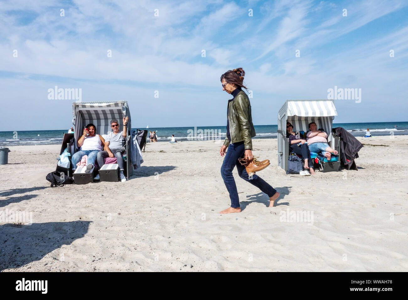 Une femme mûre marche pieds nus à travers la plage parmi les chaises de plage, les gens mer Baltique plage d'été Allemagne Warnemunde Banque D'Images