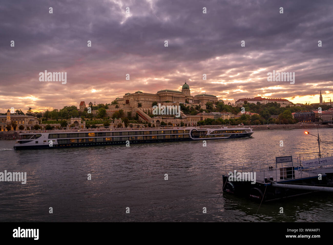 Vue du coucher de soleil du château de Buda au-dessus du Danube à Budapest en Hongrie avec une rivière passant par des navires de croisière Banque D'Images