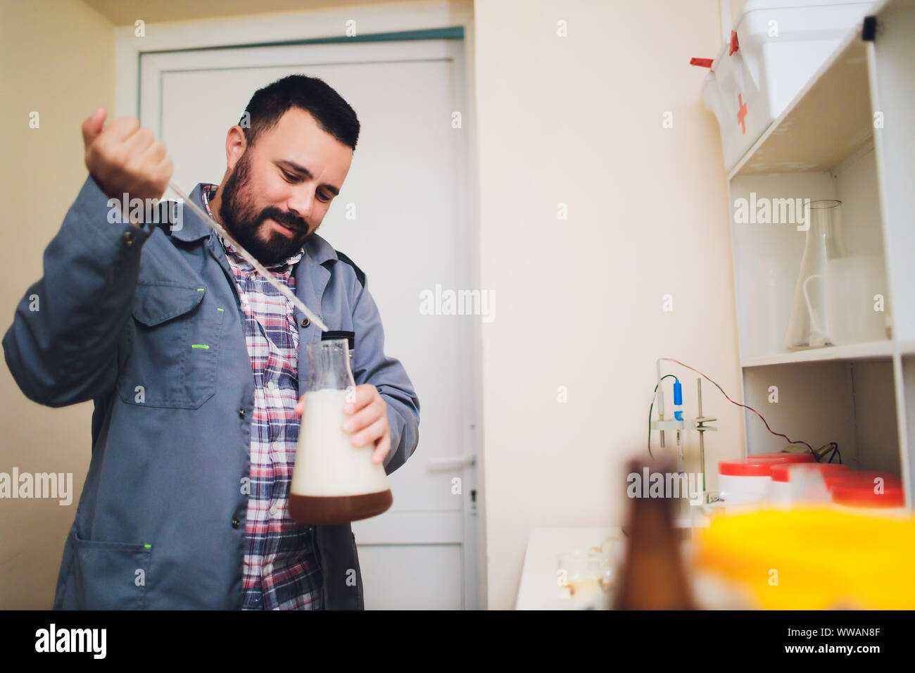 Spécialiste de la tenue de protection blanc en résille avec masque et travaillant dans l'usine d'aliments et de boissons. Spécialiste de l'homme contrôle de bouteilles pour boissons Banque D'Images