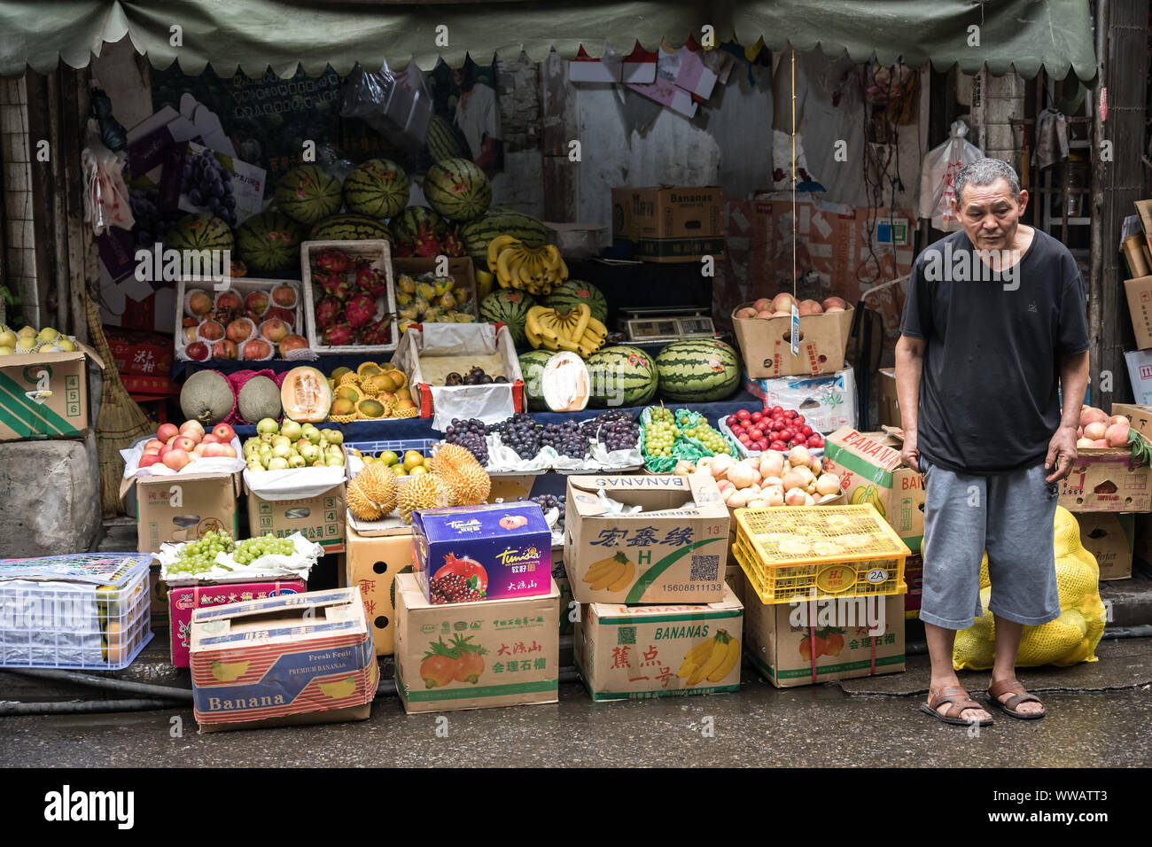 Xian, Chine - Juillet 2019 : fatigué d'un vieil homme qui se tient devant un étal de fruits et légumes dans le quartier musulman de Xi'an, province du Shaanxi ville Banque D'Images