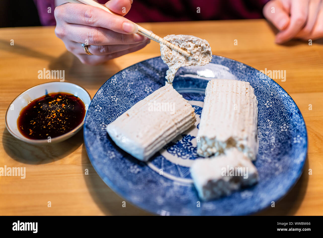 Closeup of woman holding hands traditionnel japonais tofu komo dofu en baguettes avec de la sauce soja sur la plaque sur une table en bois cuisine à Takayama, l'établissement Hida dans Banque D'Images