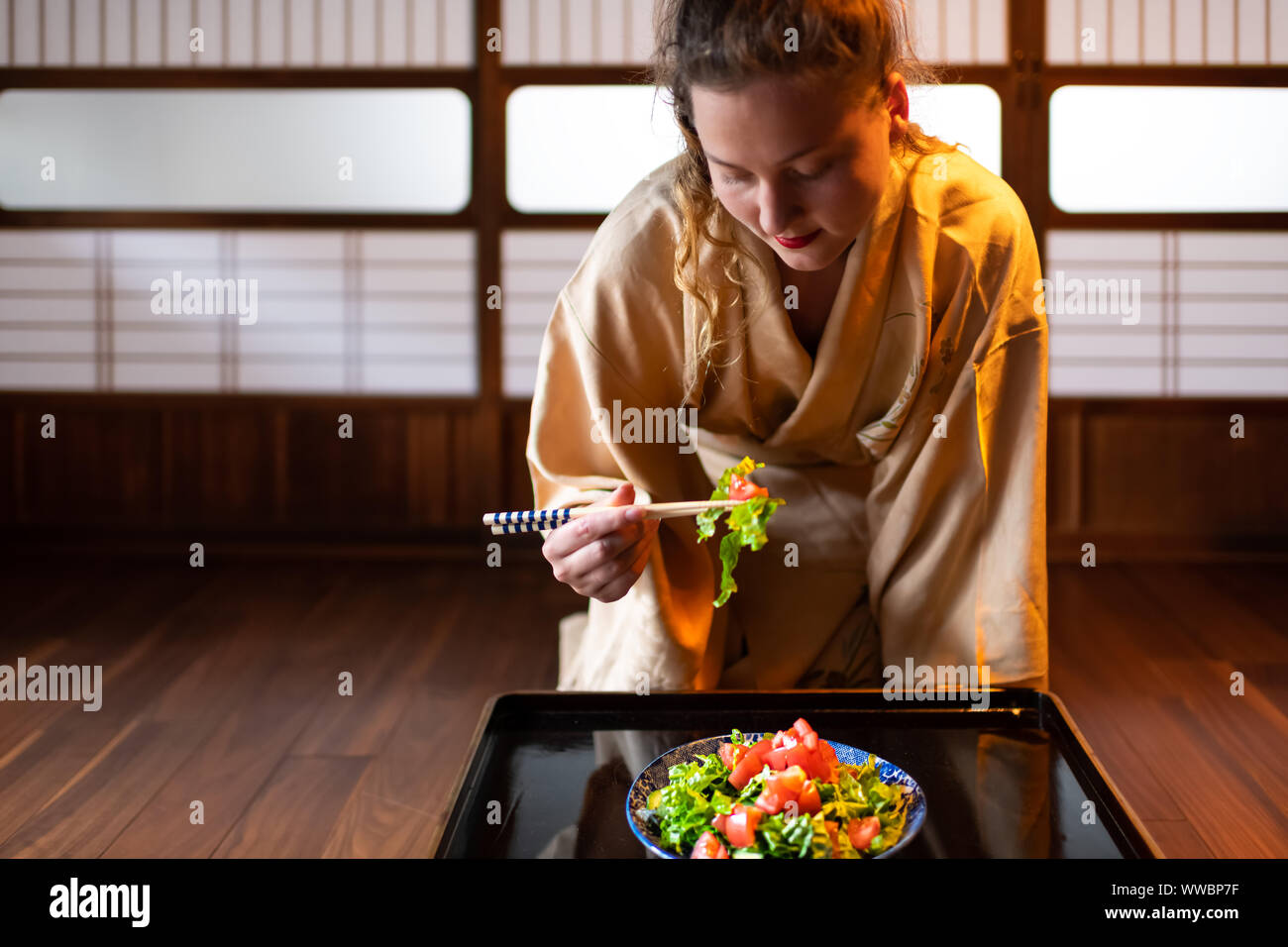 Jeune femme en kimono traditionnel japonais assis à seiza ou chambre ryokan prix par table de baguettes, mange de la salade par plaque coulissante shoji Banque D'Images