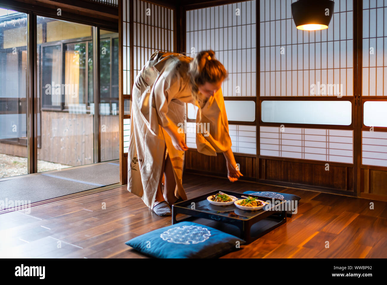 Maison traditionnelle japonaise ou ryokan avec femme jeune étranger desservant les sautés de légumes de negi, les champignons et le tofu en plaques table wi kimono Banque D'Images