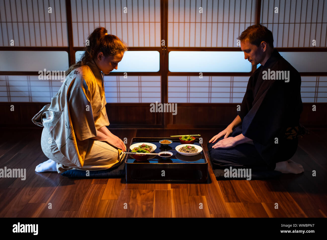 Jeune couple assis seiza sur plancher de bois franc traditionnel japonais à oreillers en ryokan soba de plats kaiseki, natto, edamame et sauce de soja sur Banque D'Images