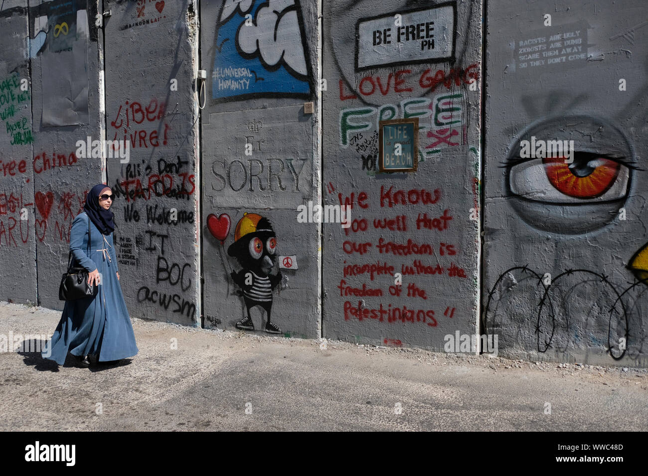 Une femme palestinienne promenades le long de la barrière de séparation ou un mur pulvérisés avec des slogans graffiti par les touristes à la périphérie de la ville de Bethléem en Cisjordanie. Territoires palestiniens, Israël Banque D'Images