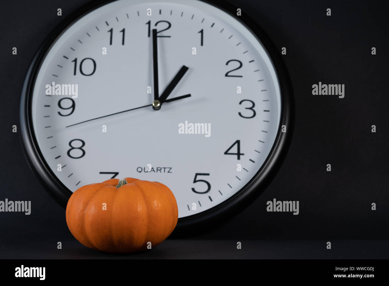 Mini pumpkin en premier plan avec big white réveil, montrant son heure de potiron avec fond noir à 13 Horloge. concept et close up. Banque D'Images