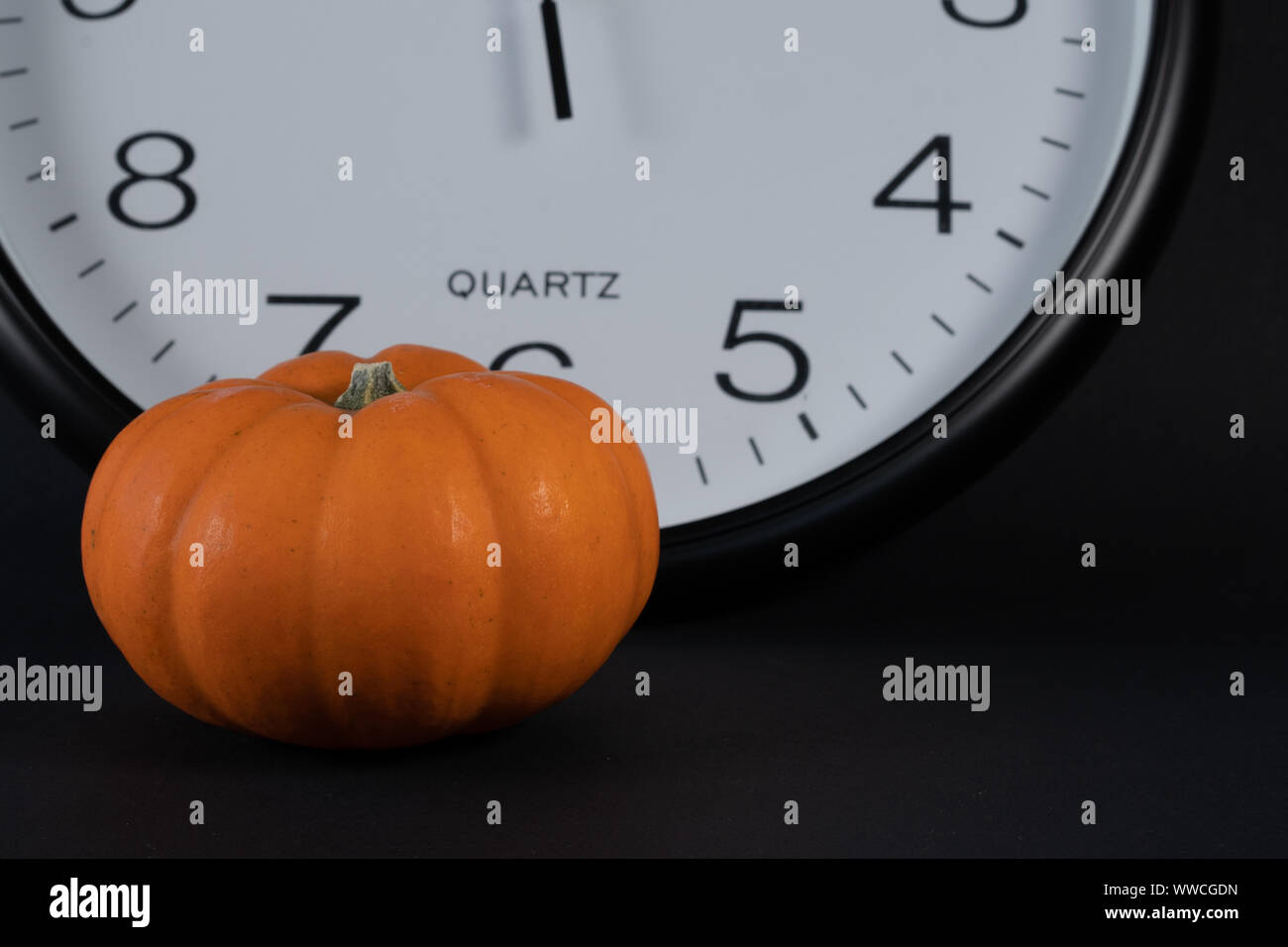 Mini pumpkin en premier plan avec big white réveil, montrant son heure de potiron avec fond noir à 13 Horloge. concept et close up. Banque D'Images