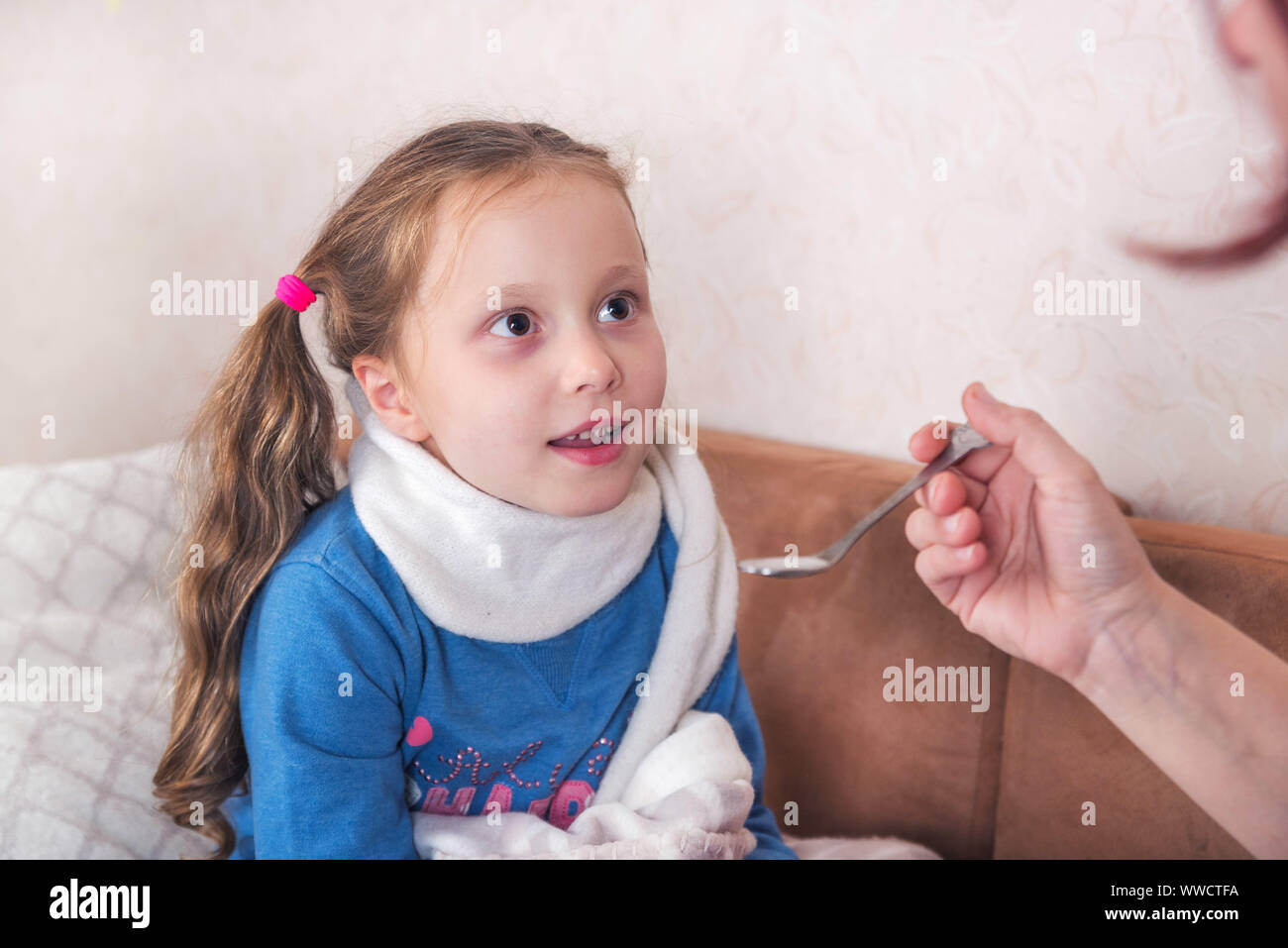 Enfant prenant la médecine. Sick girl avec écharpe lying on bed Banque D'Images