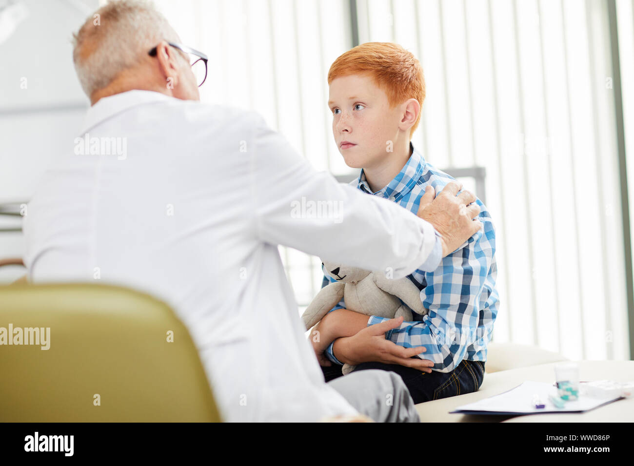 Portrait of cute red haired boy dans les cabinets de médecin principal au bureau à la recherche au cours de la consultation dans une clinique de l'enfant, copy space Banque D'Images