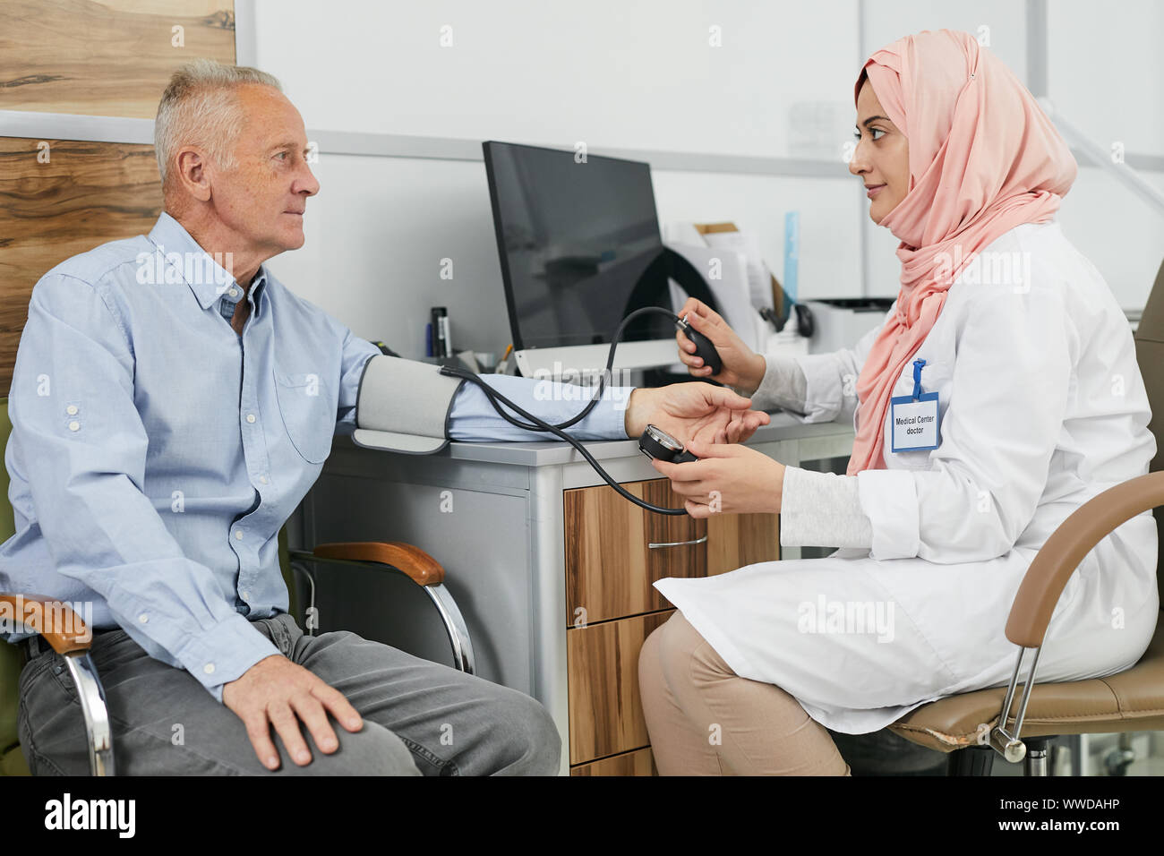 Vue de côté portrait de jeune femme arabe travailler comme médecin dans une clinique médicale et la mesure de la pression artérielle de senior patient, copy space Banque D'Images