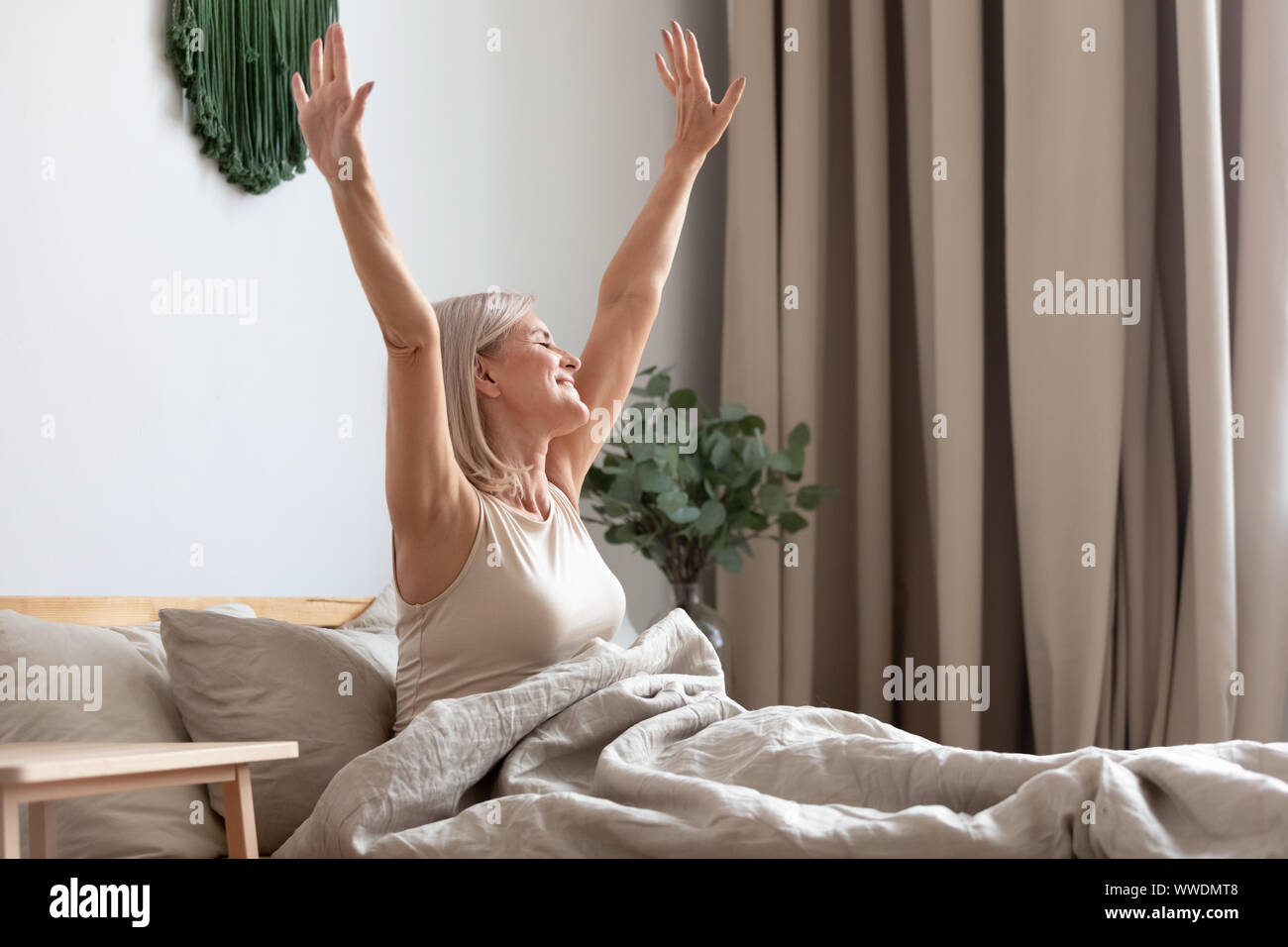 Happy woman sitting in bed, qui s'étend les mains après l'éveil Banque D'Images