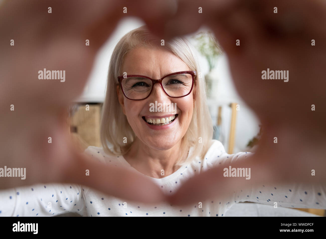 Portrait of smiling mature woman looking mains en forme de coeur Banque D'Images