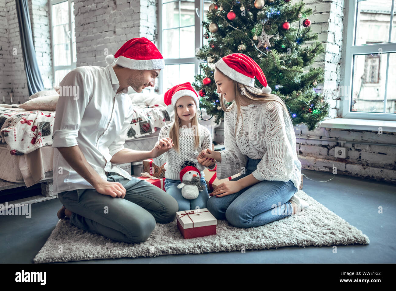 Célébration de la famille soirée de Noël. Famille trois personnes assises sous conifère arbre de Noël sur marbre de tapis de laine. Banque D'Images