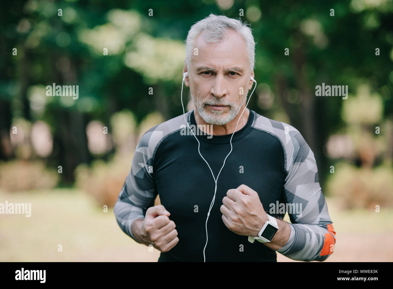 Confiant dans la musique à l'écoute de sportif à maturité en faisant du jogging dans le parc d'écouteurs Banque D'Images