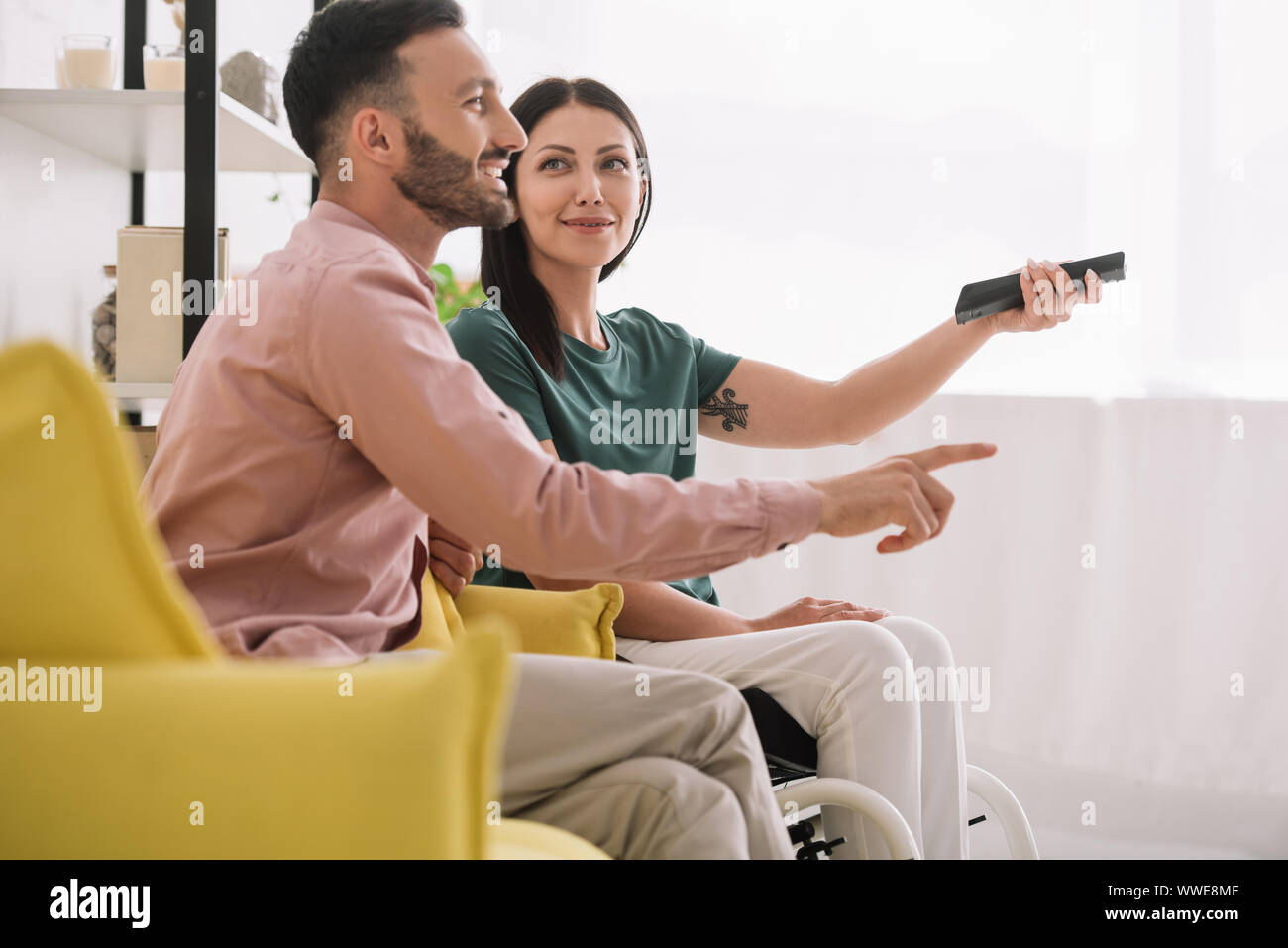 Cheerful homme pointant avec le doigt tout en regardant la tv avec mobilité petite amie Banque D'Images